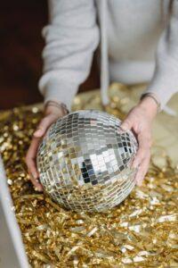 Tarotpolitan promotion picture. A photograph of two feminine hands stretching down to put a disco ball on golden tinsel.